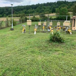 HEFEST GROUP SPÓŁKA Z OGRANICZONĄ ODPOWIEDZIALNOŚCIĄ - Teren przemysłowy z żółtymi instalacjami gazowymi po świeżo skoszonym trawniku, widoczne resztki trawy na powierzchni.