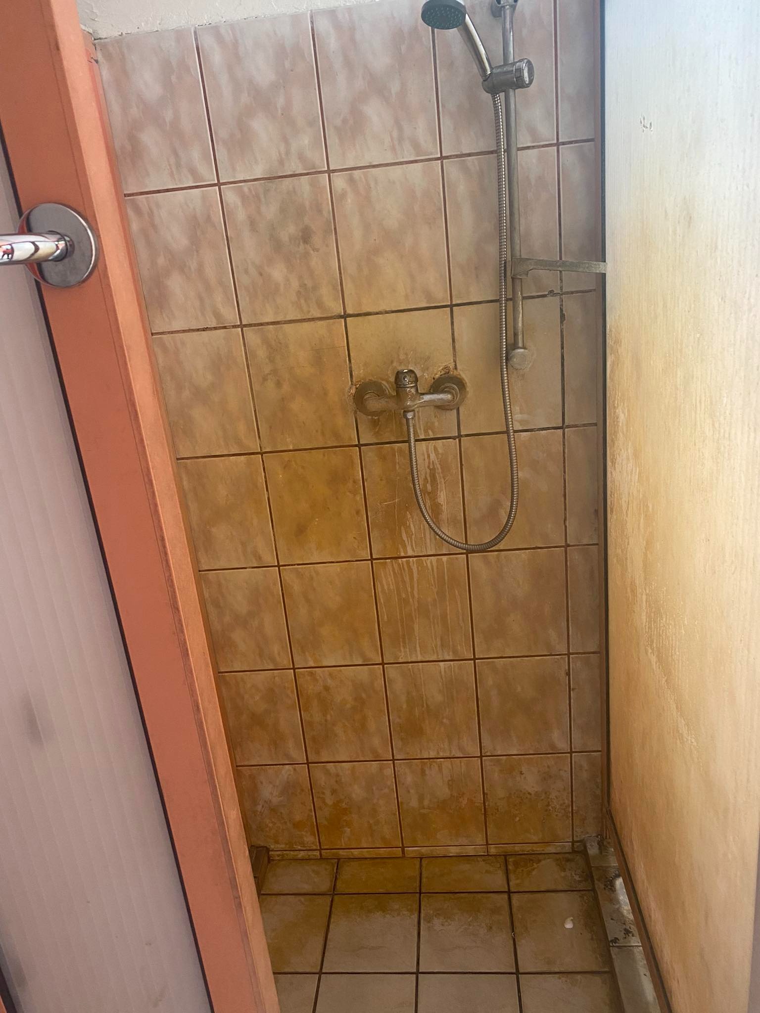 Zaniedbana kabina prysznicowa z brudnymi, brązowymi płytkami i zardzewiałą armaturą w łazience w Poznaniu, wymagająca gruntownego czyszczenia.