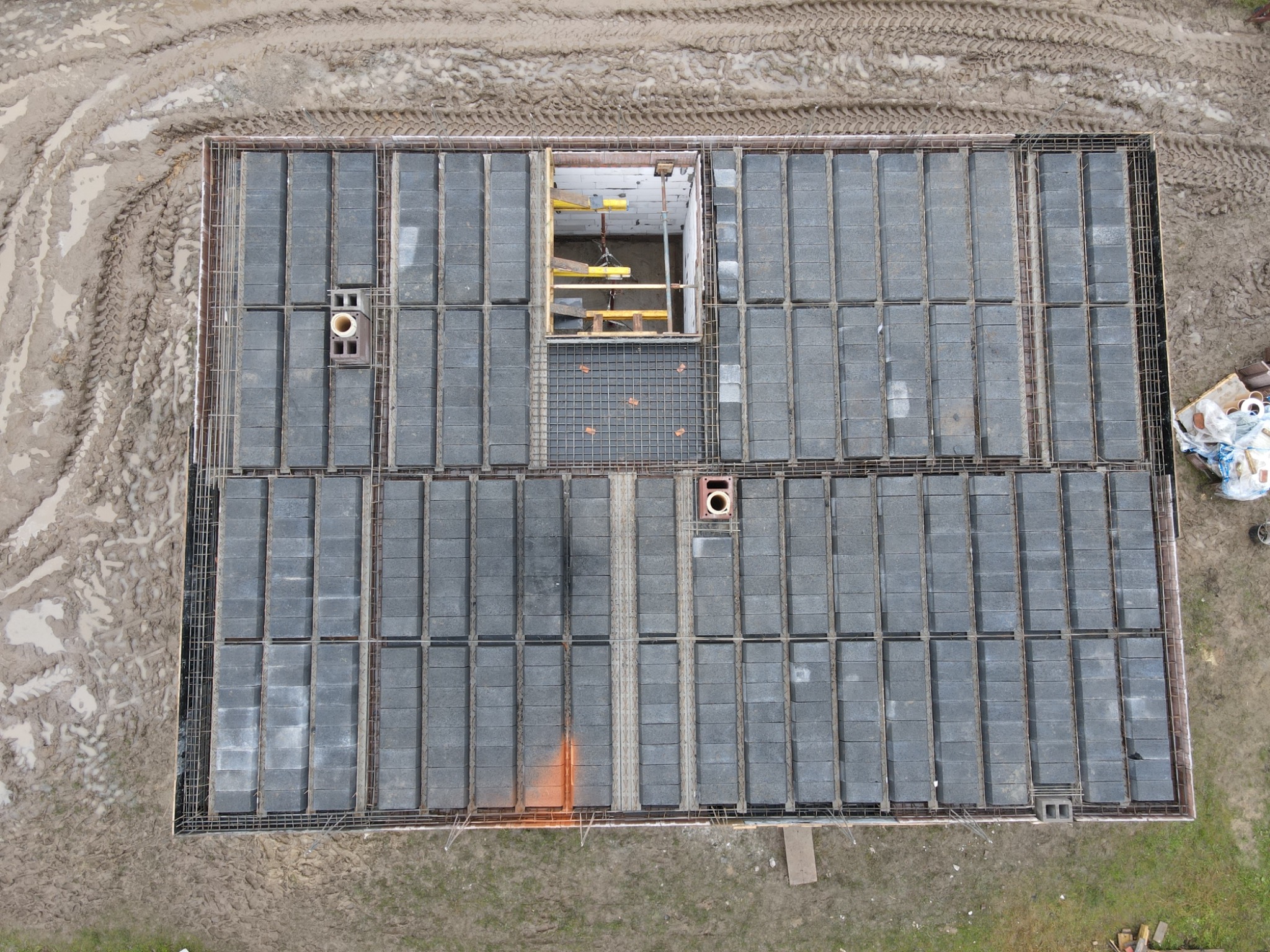Widok z góry na fundament budynku w trakcie budowy, widoczne bloczki betonowe ułożone w szalunku z prętów zbrojeniowych, fragment wykopu z widoczną konstrukcją szalunkową wewnątrz.