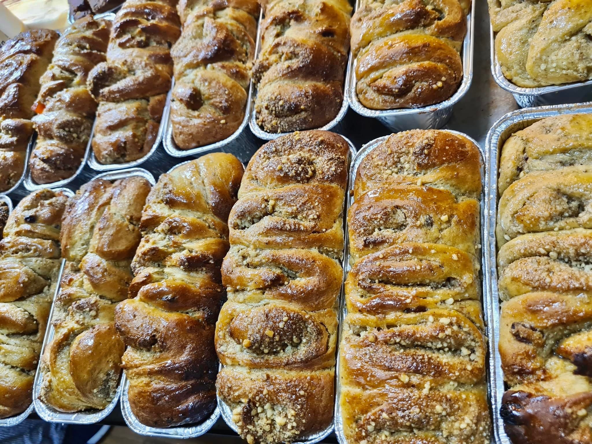 Rzędy świeżo upieczonych, błyszczących babek drożdżowych z kruszonką w aluminiowych foremkach, prezentowanych na sprzedaż.