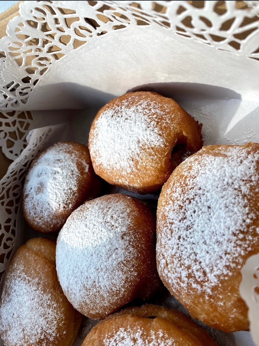 Pączki posypane cukrem pudrem ułożone w pudełku wyłożonym ozdobną serwetką.