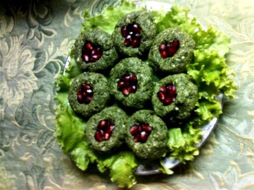 Tradycyjne gruzińskie danie Phali z orzechów włoskich, szpinaku i granatu, ułożone na liściach sałaty na talerzu, na tle wzorzystego obrusu.