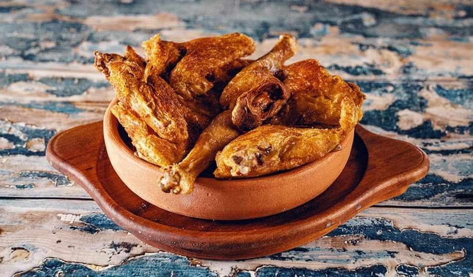 Porcja pieczonego kurczaka w ceramicznej misce na drewnianej tacy, na tle stylizowanego stołu z efektem postarzenia.