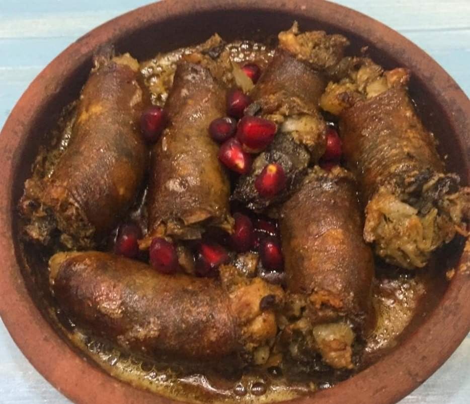 Glazurowane rolady mięsne w glinianym naczyniu, ozdobione świeżymi granatami.