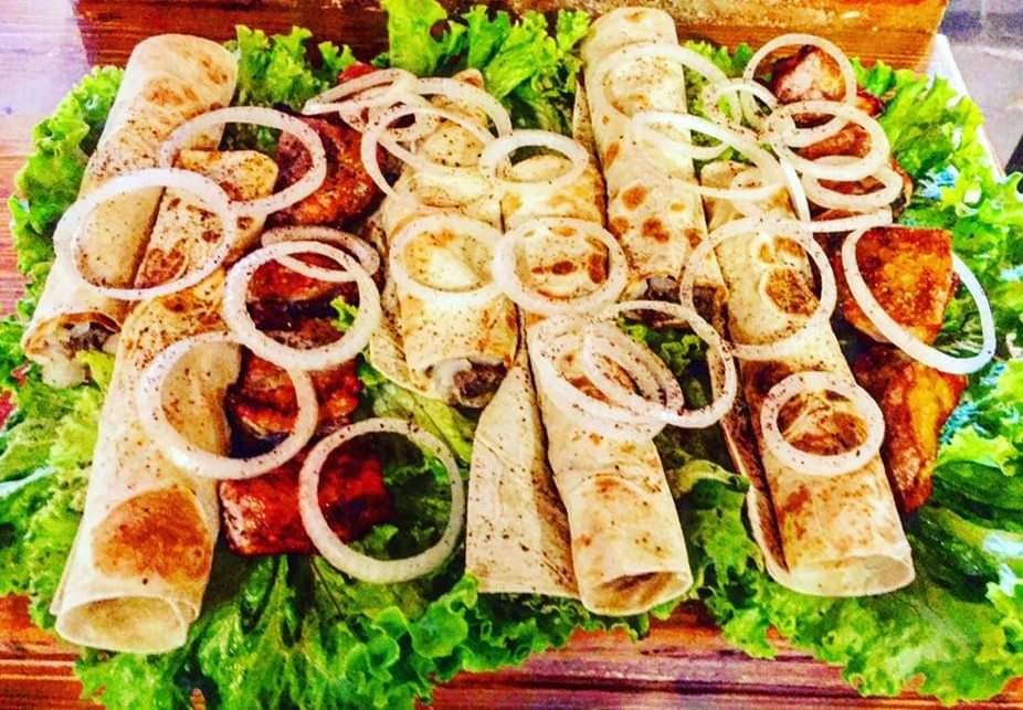 Dekoracyjnie ułożone na zielonej sałacie tortille z mięsem i krążkami cebuli na drewnianym stole.