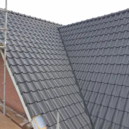 Nowy dach z ciemnoszarej dachówki ceramicznej, widok z rusztowania, fragment ocieplenia pod okapem.