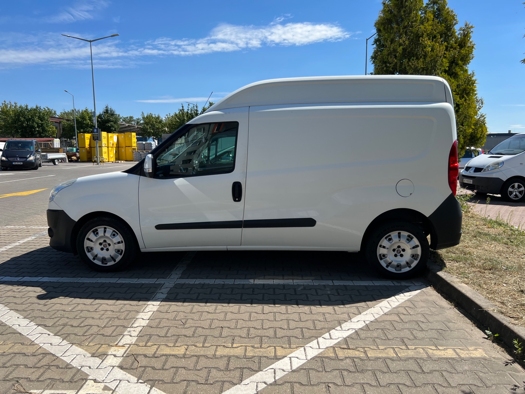 Biały, wysoki furgon na parkingu w Szczecinie, widziany z boku, z żółtymi kontenerami w tle.