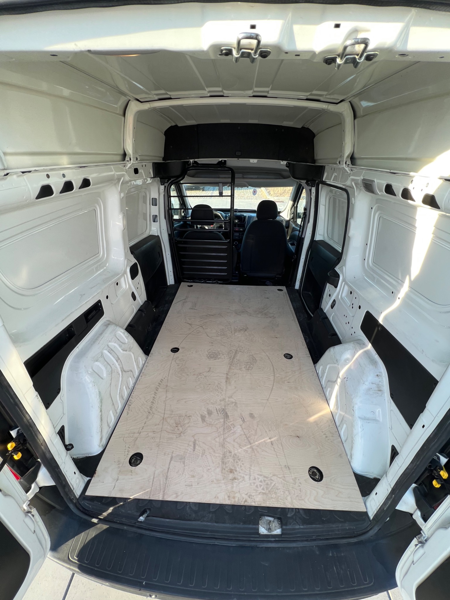 Wnętrze białego busa z drewnianą podłogą, widok od tyłu, puste przedziały ładunkowe po bokach.