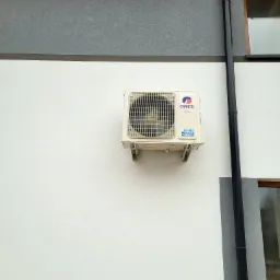 Zamontowana jednostka zewnętrzna klimatyzacji Gree na elewacji budynku z widoczną rurą spustową i oknem.