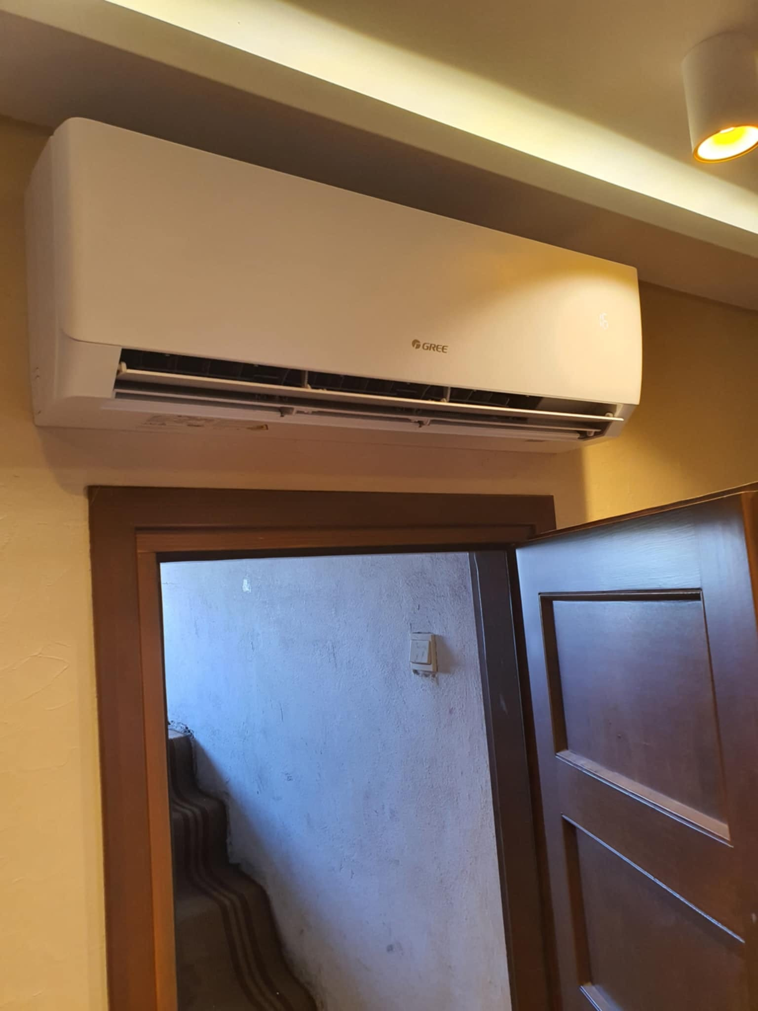 Klimatyzator GREE zamontowany nad drzwiami w pomieszczeniu z widocznymi schodami w tle.