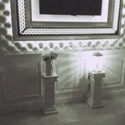 Elegancka ściana z pikowanym panelem, podświetlonym obramowaniem telewizora i dekoracyjnymi kolumnami z wazonem i lampą, utrzymana w monochromatycznej tonacji.