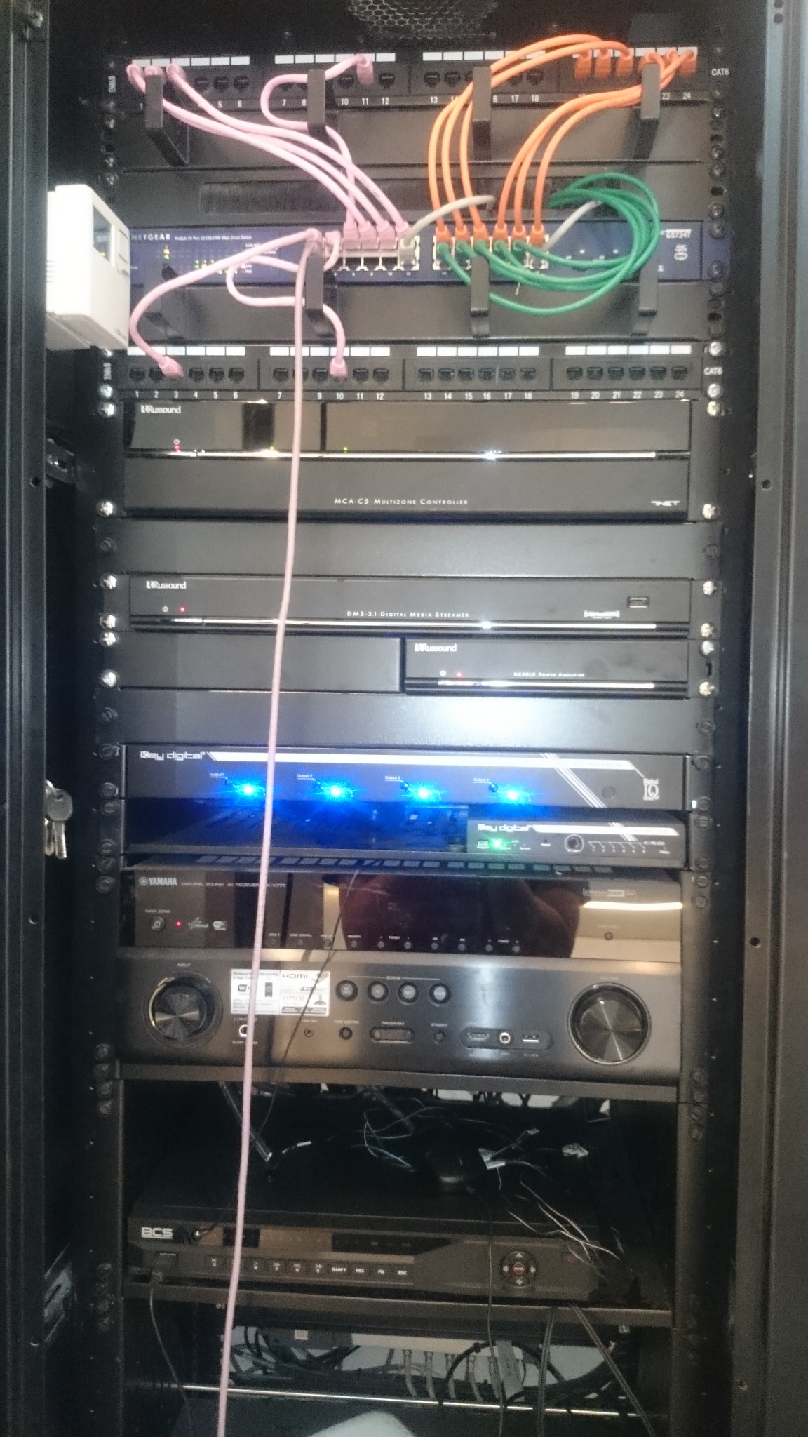 Rack serwerowy z zainstalowanym sprzętem audio i sieciowym: router Netgear, kontroler strefowy Russound MCA-C5, streamer multimedialny Russound DMS-3.1, wzmacniacz mocy Russound D250LS, odtwarzacz...