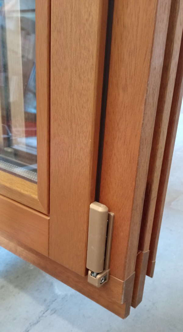 Drewniane okno składane z widocznym mechanizmem składania i uszczelką, zbliżenie na narożnik i zawias.