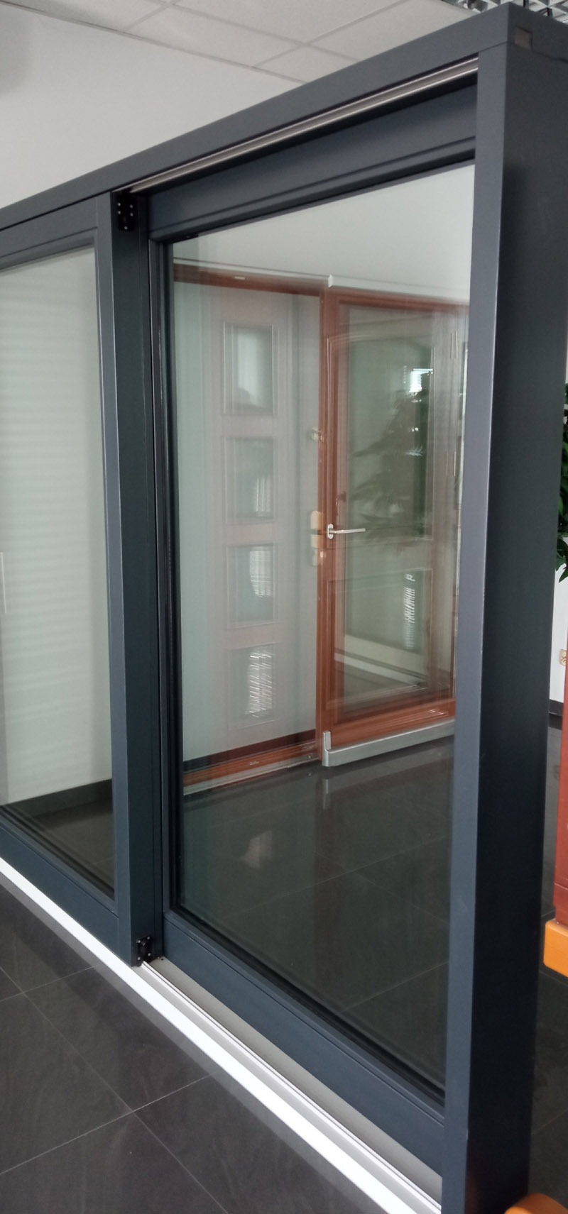 Szare aluminiowe drzwi przesuwne z widocznym mechanizmem przesuwnym i odbiciem drzwi wewnętrznych w szybie.
