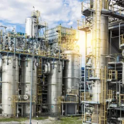 Kompleksowa instalacja przemysłowa z metalowymi zbiornikami, rurami, schodami i platformami w słoneczny dzień.