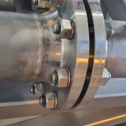 Szczegółowe ujęcie z bliska złącza kołnierzowego rurociągu ze stali nierdzewnej, z widocznymi śrubami i spawami.