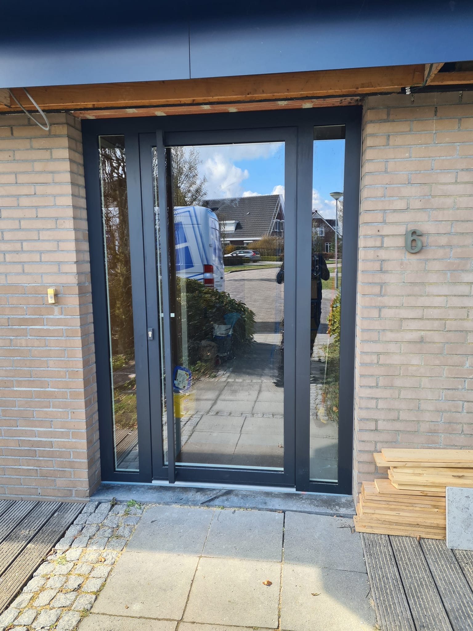 Zamontowane, przesuwne okno balkonowe z ciemną ramą w ścianie z cegły; widoczne prace wykończeniowe i odblask samochodu w szybie.