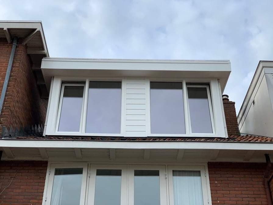 Białe okna na poddaszu z widocznymi elementami konstrukcyjnymi, ceglana ściana budynku z boku.