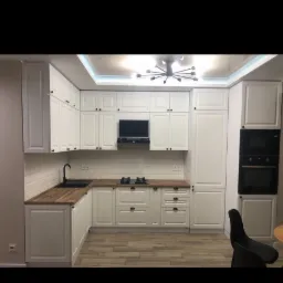 Jasna kuchnia z drewnianym blatem, czarną armaturą i piekarnikiem w zabudowie, oświetlona lampą sufitową.