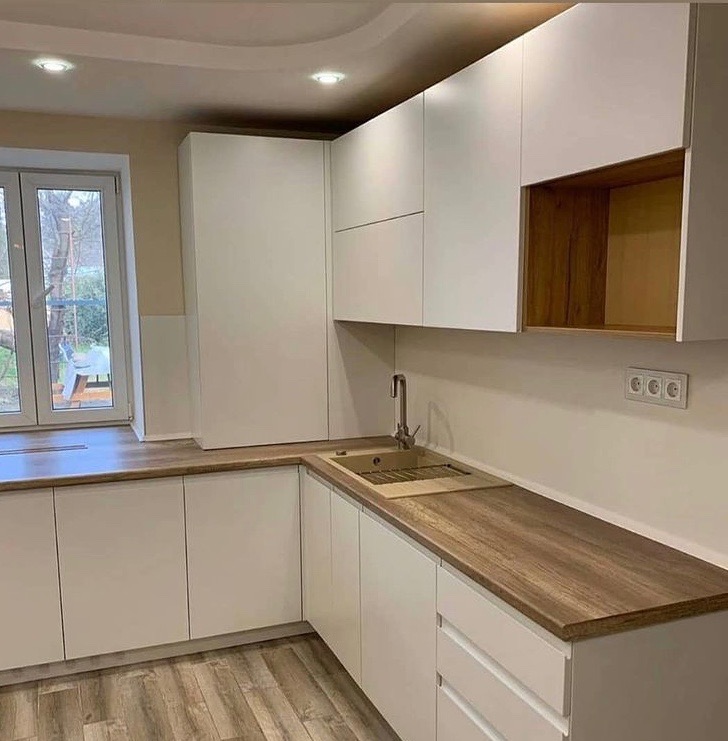 Nowoczesna, biała kuchnia na wymiar z drewnianymi blatami i otwartą półką z drewnianym wnętrzem, widok na okno