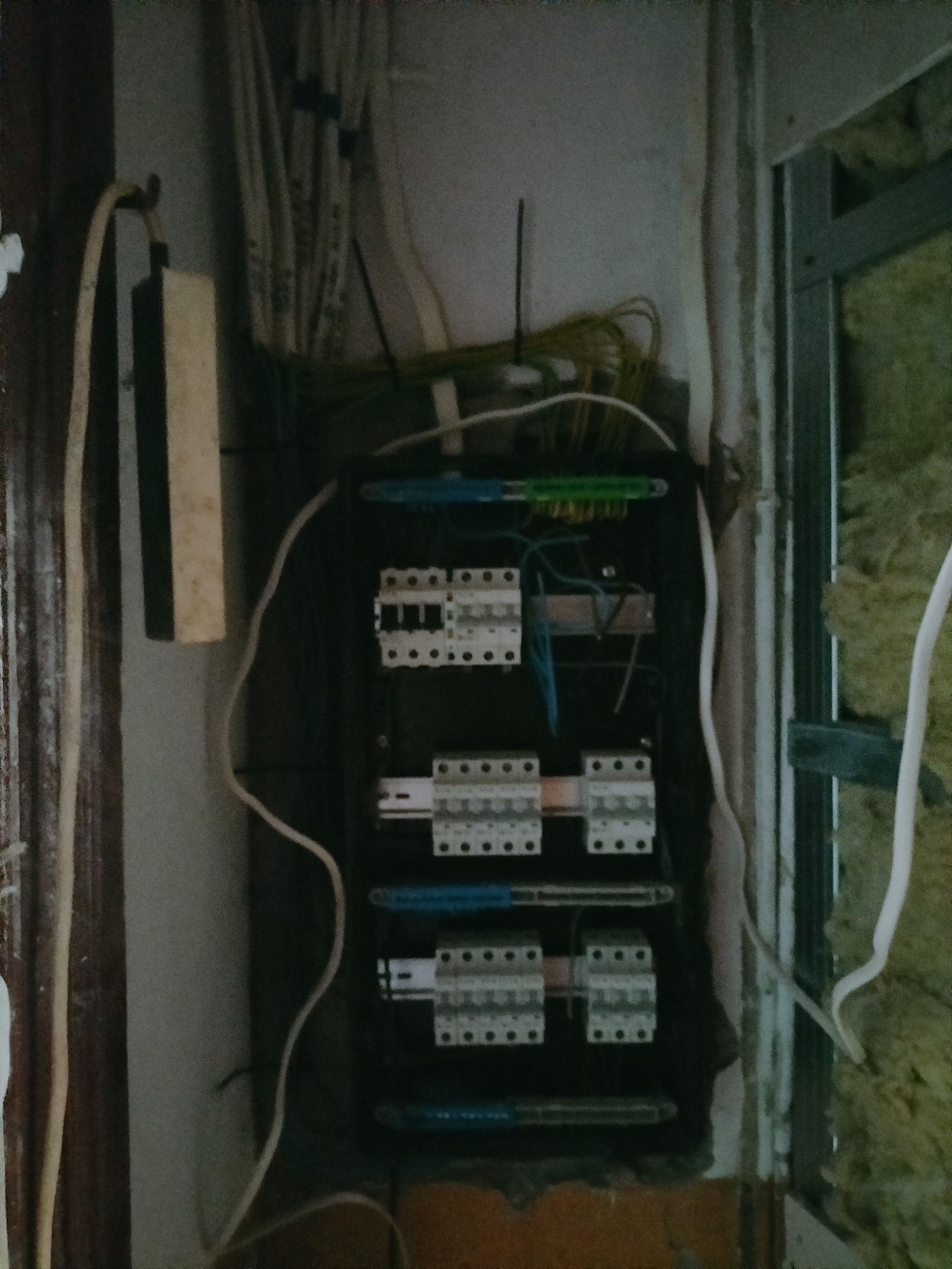 Rozdzielnica elektryczna z przewodami w trakcie montażu w Katowicach. Widoczne zabezpieczenia i przewody w ścianie. Prace instalacyjne w surowym wnętrzu.