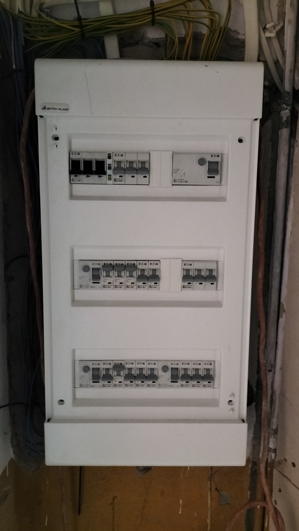 Rozdzielnia elektryczna Elektro-Plast z wyłącznikami Eaton, zamontowana na ścianie z widocznymi przewodami. Widok z przodu, oświetlenie dzienne.