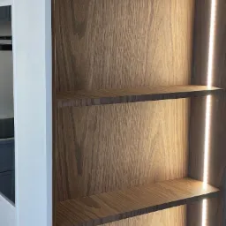Półki z drewna orzechowego z wbudowanym oświetleniem LED, biały bok szafy widoczny z lewej strony.