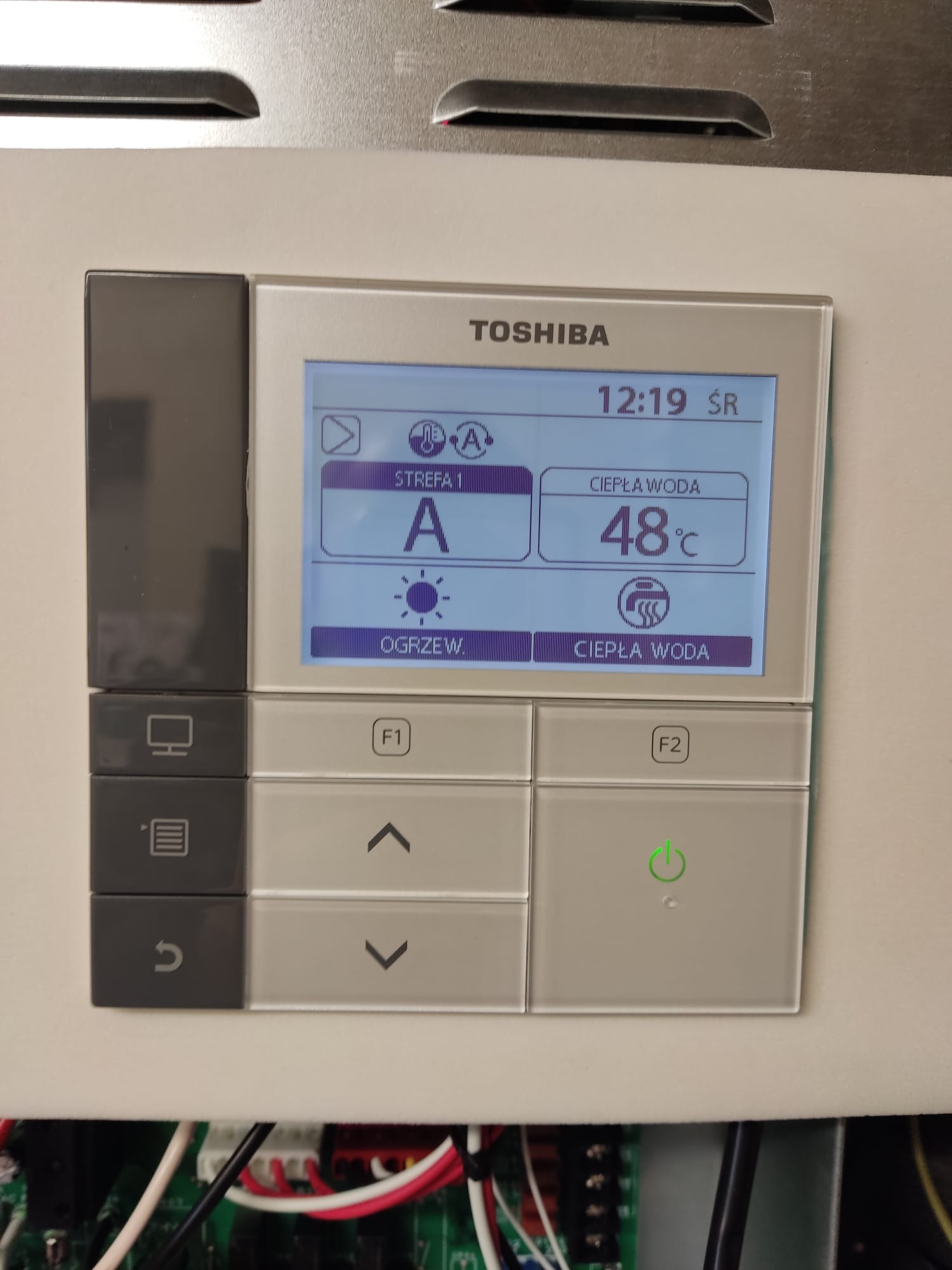 Panel sterowania pompy ciepła Toshiba z wyświetlaczem LCD pokazującym ustawienia strefy 1, temperaturę ciepłej wody 48 stopni Celsjusza oraz aktualny czas 12:19, widoczne przyciski funkcyjne F1...