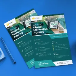 Dwa identyczne foldery reklamowe agencji digital marketingowej leżące na niebieskim tle, obok niebieskiego długopisu i fragmentu zegara.