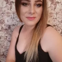 Portret kobiety z profesjonalnym makijażem oczu i ust, z włosami ombre i w czarnym topie na tle tapety w róże.