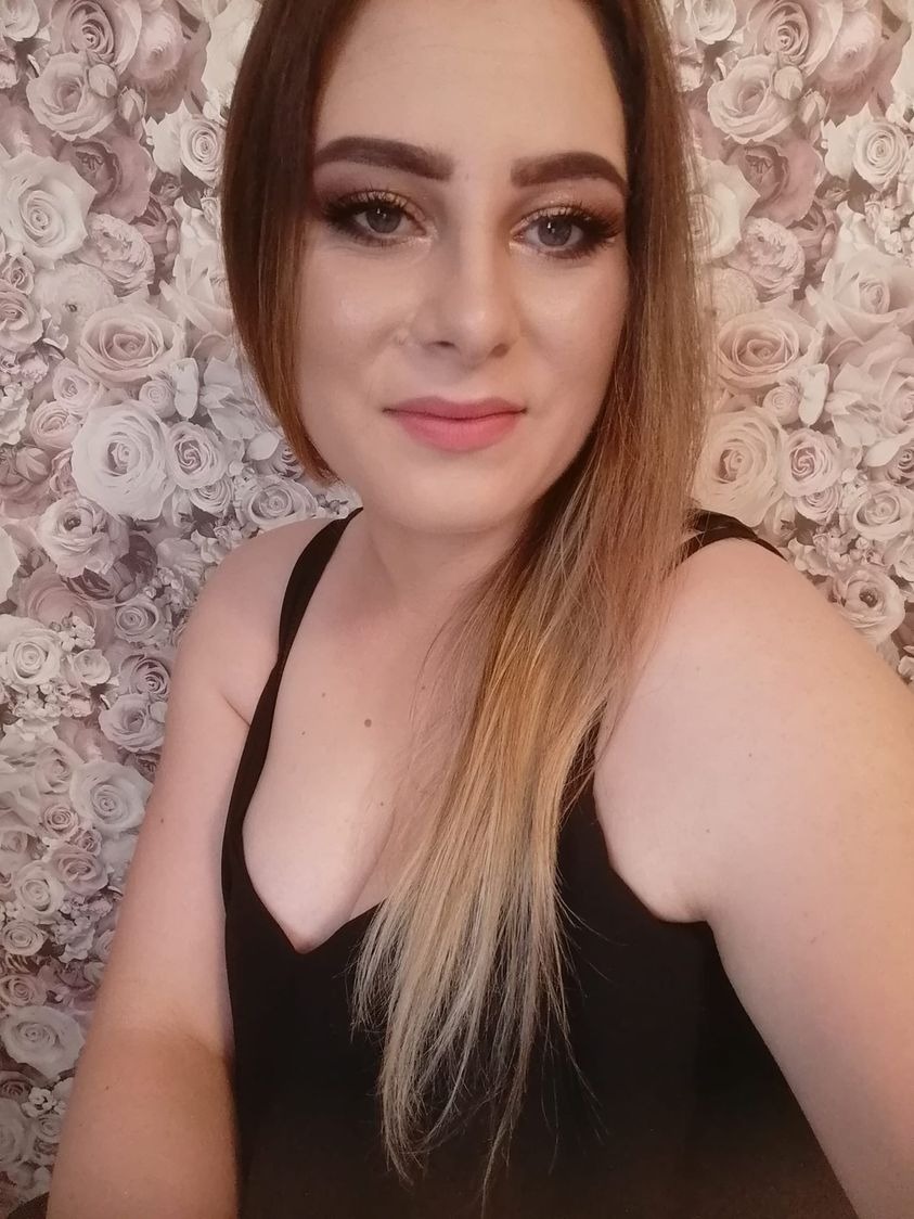 Portret kobiety z profesjonalnym makijażem oczu i ust, z włosami ombre i w czarnym topie na tle tapety w róże.