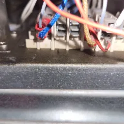 Widok z bliska na wewnętrzne okablowanie i złącza elektryczne urządzenia AGD, prawdopodobnie podczas naprawy lub konserwacji, z widocznymi przewodami w izolacji czerwonej i niebieskiej.