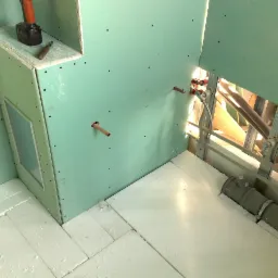 Poddasze w trakcie adaptacji: zielone płyty karton-gips na ścianach, izolacja podłogi z polistyrenu ekstrudowanego, widoczne rury instalacji wodnej i kanalizacyjnej, wiertarka i nóż na zabudowie.