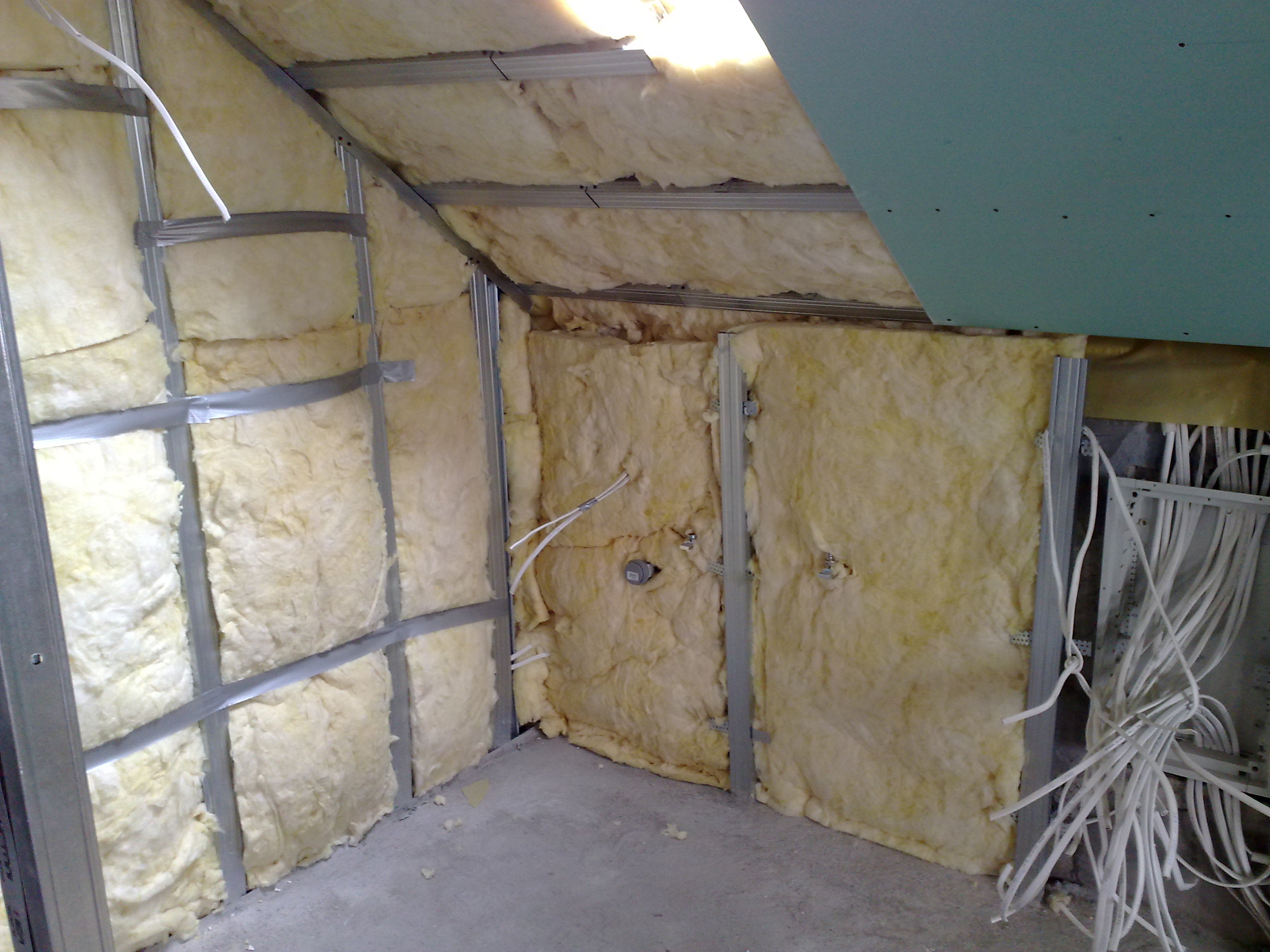 Adaptacja poddasza: izolacja ścian wełną mineralną w metalowym stelażu, widoczne przewody elektryczne i fragment płyty gipsowo-kartonowej na suficie.