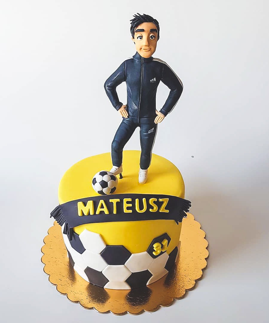 Tort urodzinowy z figurką piłkarza w dresie, z piłką i napisem 'Mateusz', na złotym podkładzie.