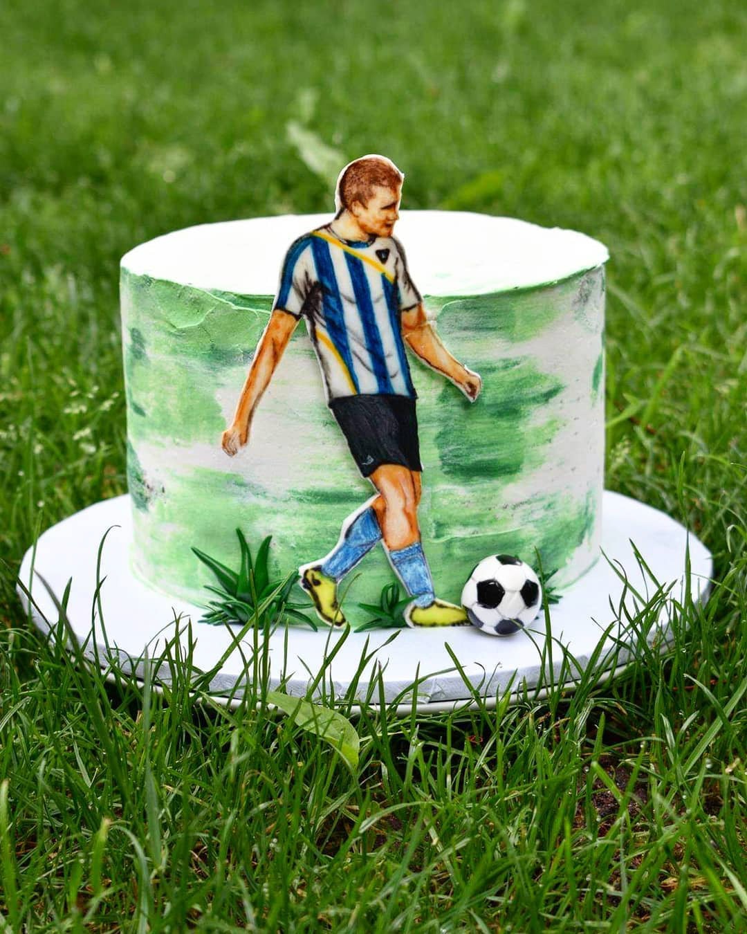 Tort zdobiony motywem piłkarskim: ręcznie malowany tort z figurką piłkarza i piłką, ustawiony na trawie.