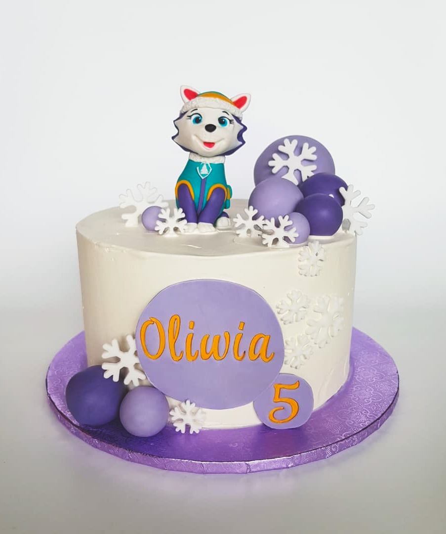 Tort urodzinowy z figurką pieska z bajki Psi Patrol, imieniem Oliwia i cyfrą 5, ozdobiony fioletowymi kulkami i białymi płatkami śniegu na fioletowej podkładce.
