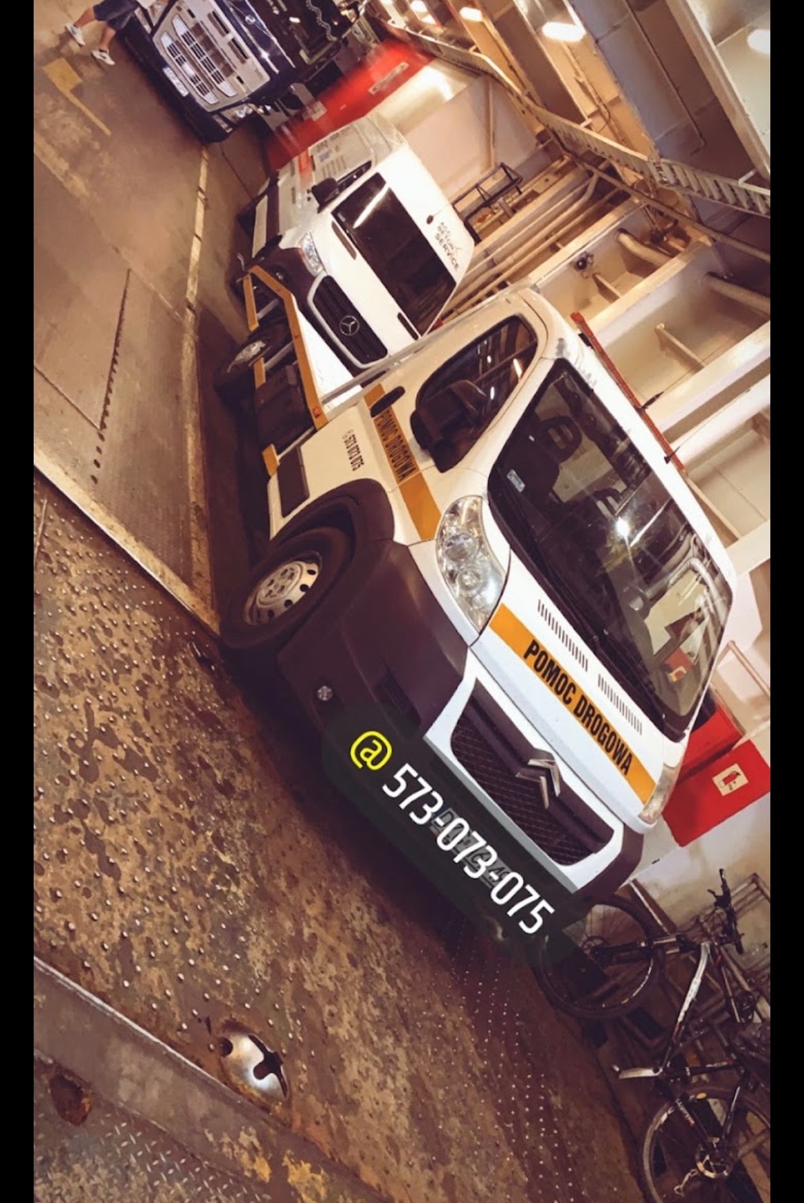 Laweta 'Pomoc Drogowa' marki Citroen, zaparkowana wewnątrz promu, z widocznym numerem telefonu i rowerami w tle.