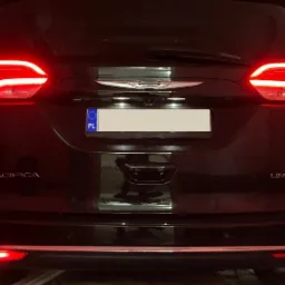 Tył czarnego samochodu Chrysler Pacifica Limited z włączonymi światłami hamowania, widoczne tablice rejestracyjne (polska i niemiecka), logo firmy Moto Wizards w prawym dolnym rogu.