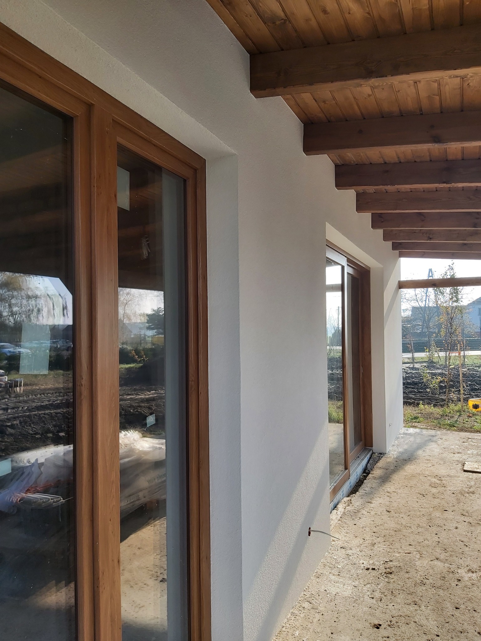 Elewacja domu po ociepleniu z drewnianą konstrukcją zadaszenia tarasu i oknami z drewnianymi ramami, widok z zewnątrz.