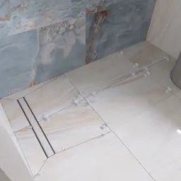Łazienka w trakcie układania płytek podłogowych i ściennych z marmurowym wzorem, widoczny odpływ liniowy i krzyżyki dystansowe.