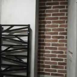 Łazienka z grzejnikiem drabinkowym w kolorze czarnym, ściana z cegły dekoracyjnej i szare płytki ceramiczne.