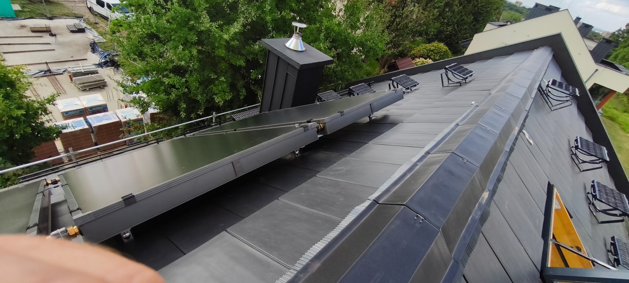 Montaż paneli słonecznych na dachu z czarnej blachy, widok z góry, z elementami rusztowania i zieleni w tle. Nowoczesne rozwiązanie energetyczne.