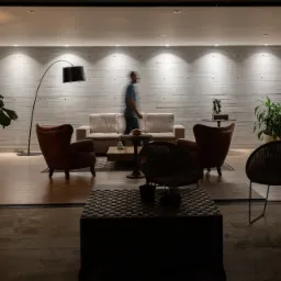 Przestronne wnętrze salonu z betonową ścianą, oświetleniem punktowym i nowoczesnymi meblami, częściowo widoczne przez otwarte przesuwne drzwi.