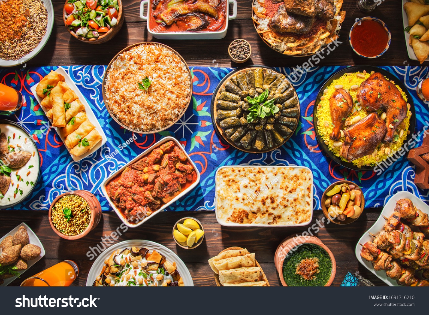 Bogaty wybór dań kuchni bliskowschodniej ułożonych na niebieskim bieżniku z geometrycznym wzorem, obejmujący pieczonego kurczaka na ryżu, gołąbki, szaszłyki, warzywa i inne tradycyjne potrawy...