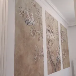 Ściana z tapetą w stylu vintage z motywem kwiatowym, podzielona na trzy panele, widoczna z perspektywy bocznej, obok biała ściana z włącznikiem światła i fragment białej futryny drzwi.