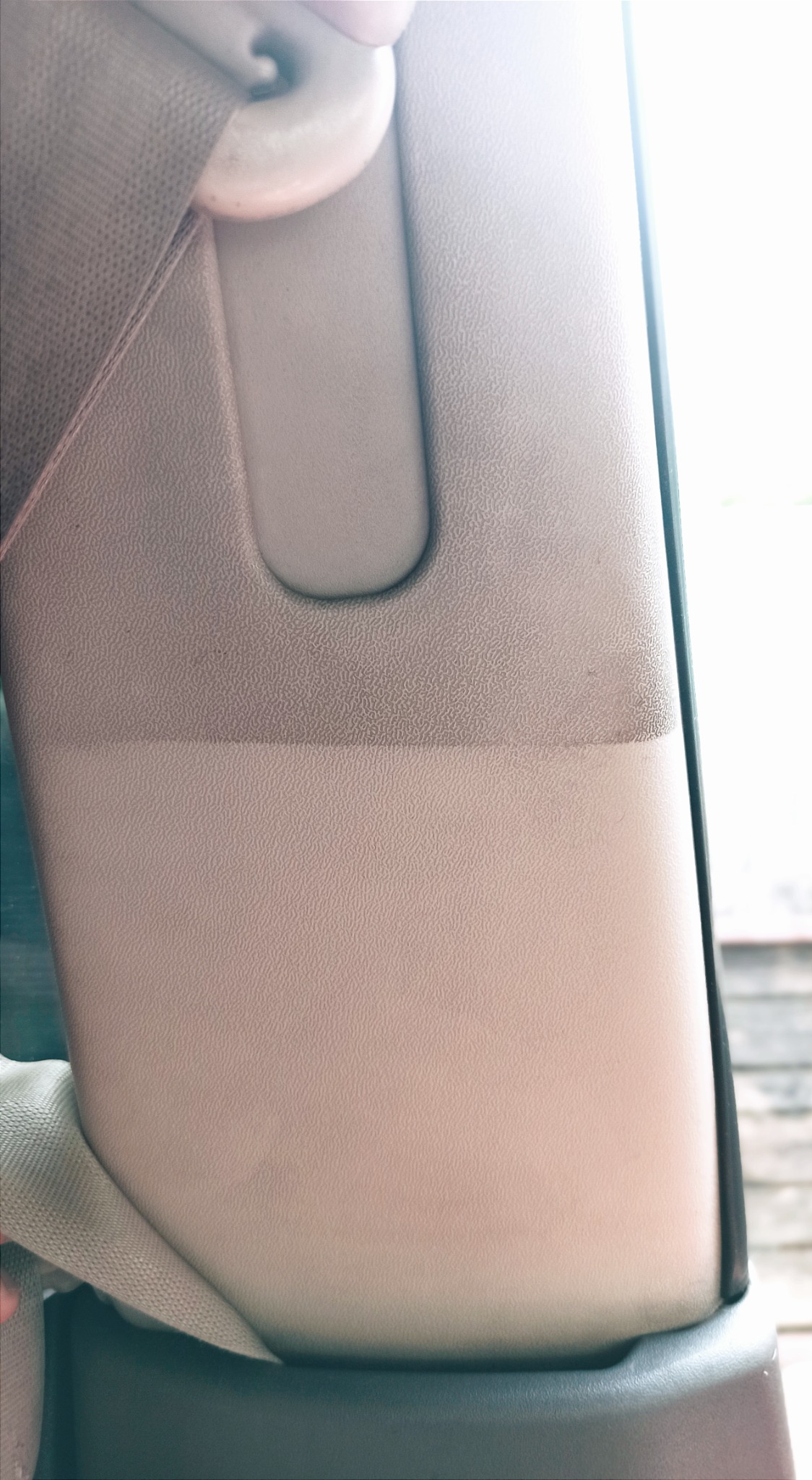 Fragment tapicerki samochodowej w jasnym odcieniu beżu z widoczną różnicą w czystości przed i po czyszczeniu, z zapięciem pasa bezpieczeństwa w tle.