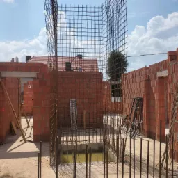 Zbrojenie pionowe w wykopie, przygotowane do zalania betonem, widoczne ściany z czerwonej cegły dziurawki i niebo z chmurami w tle.