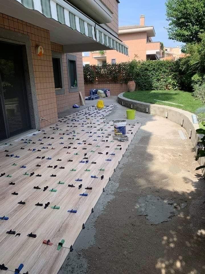 Układanie płytek na tarasie zewnętrznym domu jednorodzinnego, widoczne klipsy poziomujące i wiadro z zaprawą.