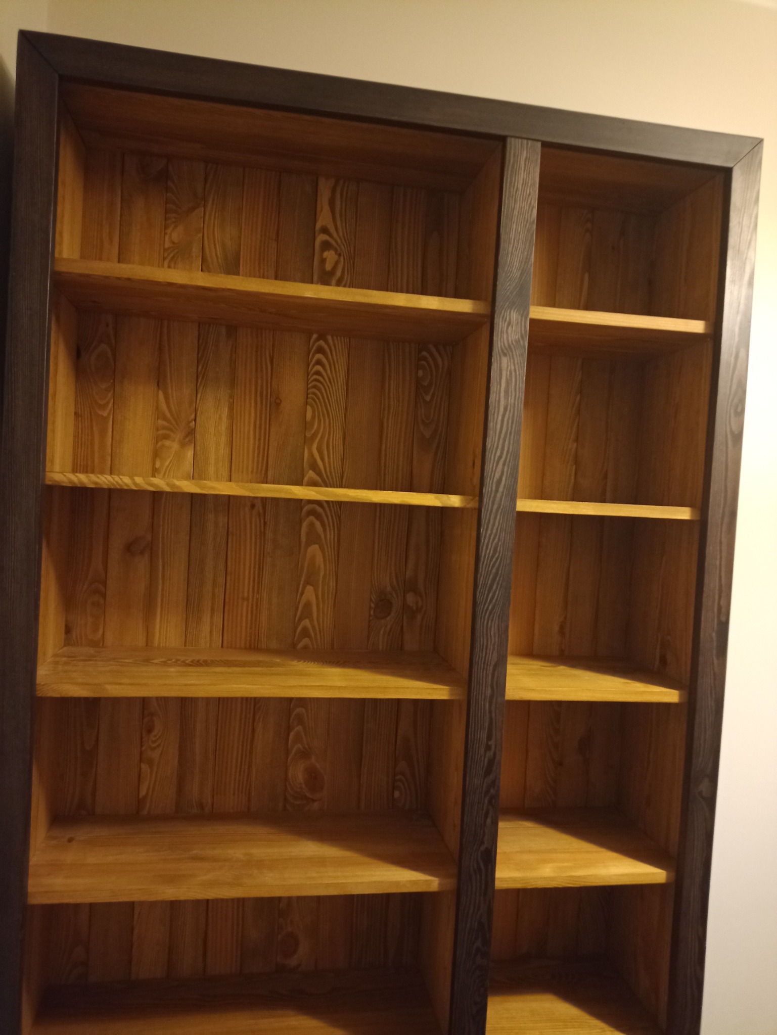 Półki w regale wykonane z jasnego drewna, zamknięte w ciemnobrązowej ramie, widoczne słoje drewna i naturalna faktura.